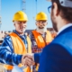 Construction worker in protective uniform shaking hands with businessman in hardhat at construction