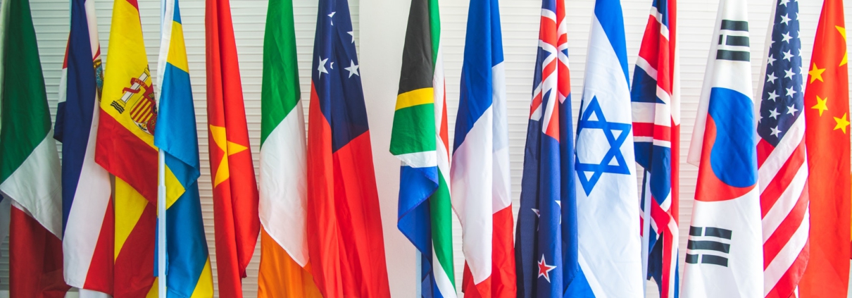 collection of various flags of different countries standing tall together in a row on a stand