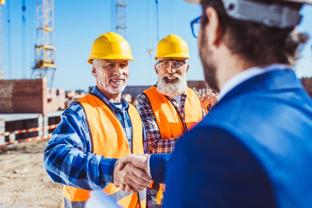 Construction worker in protective uniform shaking hands with businessman in hardhat at construction