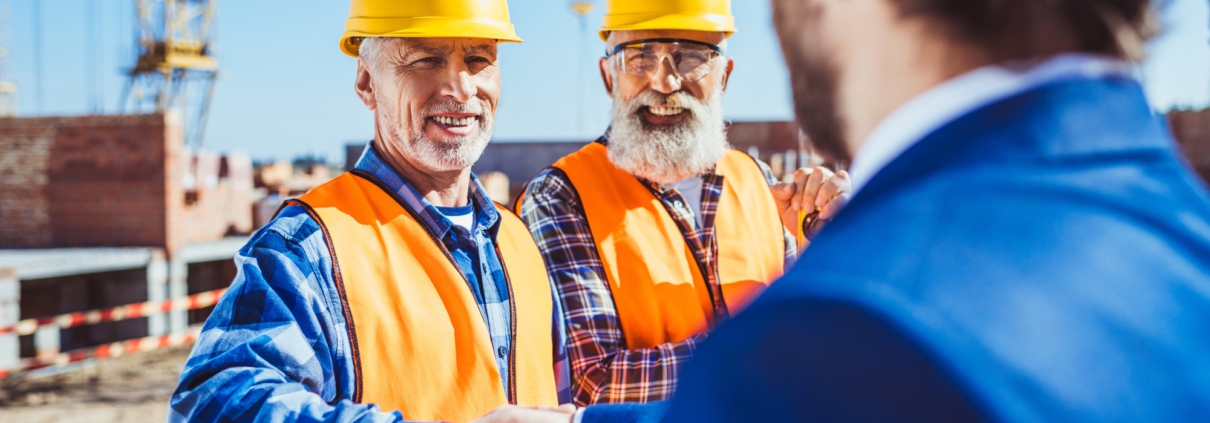 Construction worker in protective uniform shaking hands with businessman in hardhat at construction