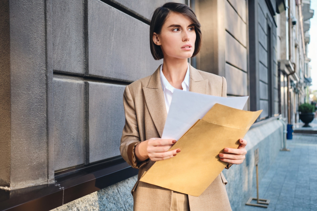 Young serious businesswoman in suit intently looking away working with papers on street