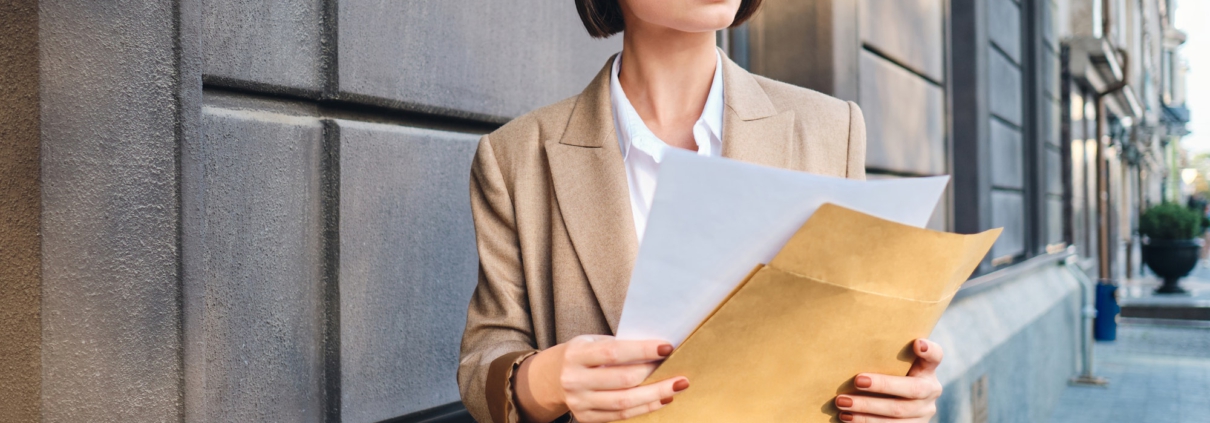 Young serious businesswoman in suit intently looking away working with papers on street