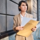 Young serious businesswoman in suit intently looking away working with papers on street